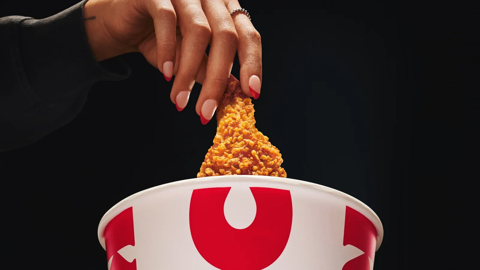 手将炸鸡放入红白KFC炸鸡桶中