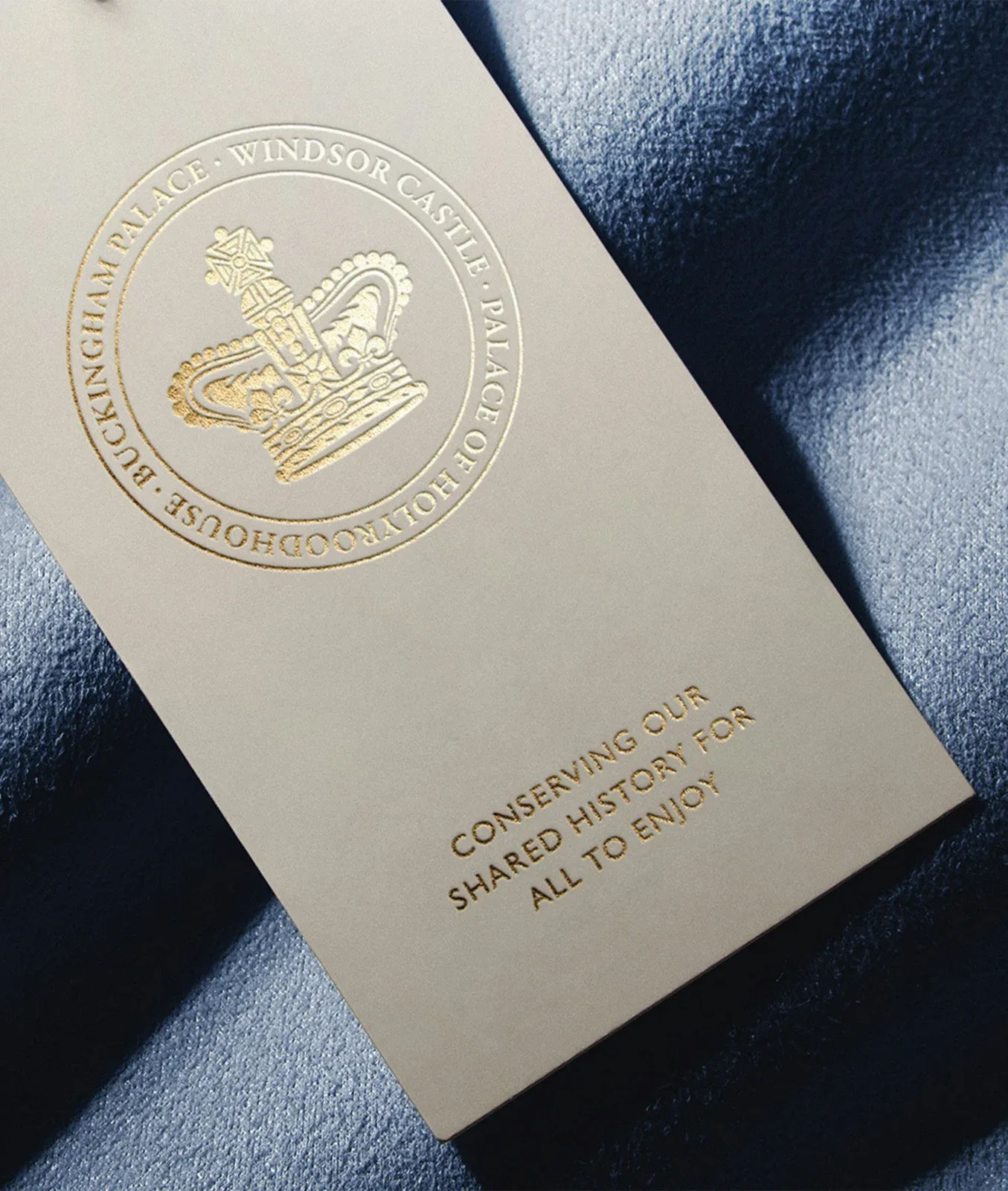 浅色卡片印有金色Royal Collection Trust徽章和文字，置于深蓝织物上。